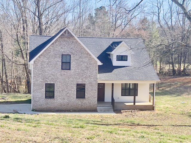 view of front facade featuring brick siding, a porch, a front yard, and roof with shingles