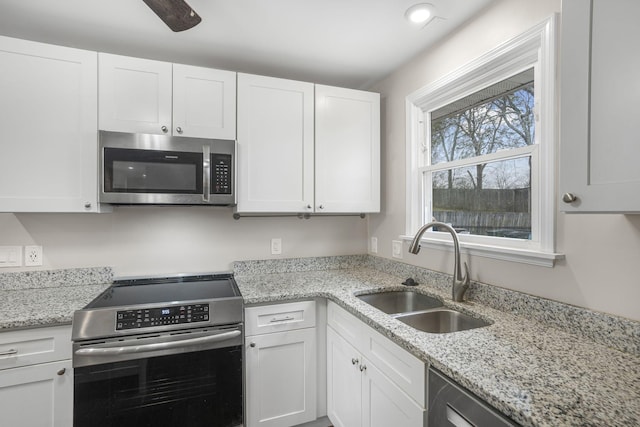 kitchen featuring light stone counters, white cabinetry, stainless steel appliances, and a sink