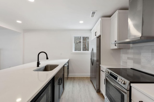 kitchen with stainless steel appliances, light countertops, wall chimney range hood, and a sink