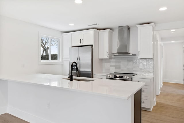 kitchen with light wood-style floors, appliances with stainless steel finishes, white cabinets, wall chimney range hood, and decorative backsplash