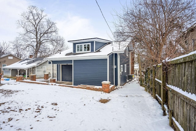 snow covered house featuring central AC unit, fence, a garage, and a chimney