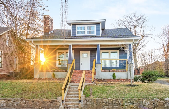 bungalow-style house with stairway, a porch, a chimney, a front lawn, and central air condition unit