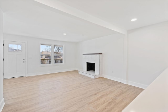 unfurnished living room featuring recessed lighting, light wood-style flooring, baseboards, and a fireplace with raised hearth