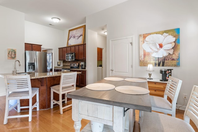 kitchen with light stone counters, appliances with stainless steel finishes, light wood-style floors, a sink, and a kitchen breakfast bar