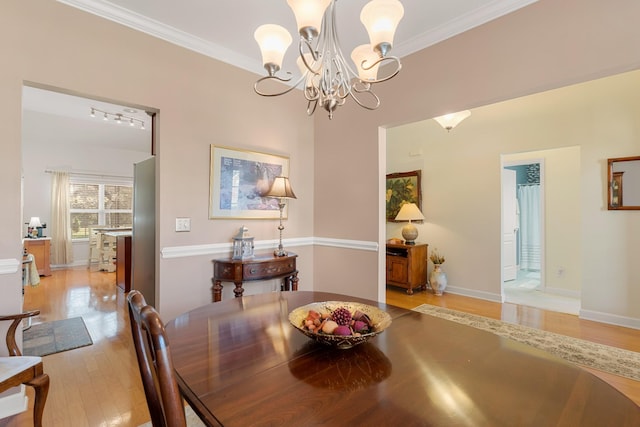 dining room featuring ornamental molding, a chandelier, light wood-style floors, and baseboards