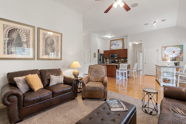 living room featuring light wood finished floors, ceiling fan, visible vents, and vaulted ceiling