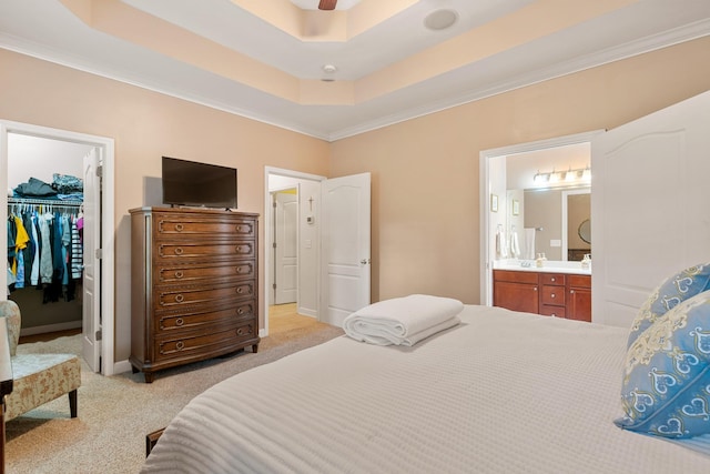 bedroom with ensuite bathroom, light carpet, a closet, a tray ceiling, and a walk in closet