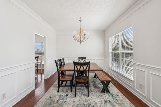 dining area featuring a decorative wall, a textured ceiling, dark wood-type flooring, and an inviting chandelier