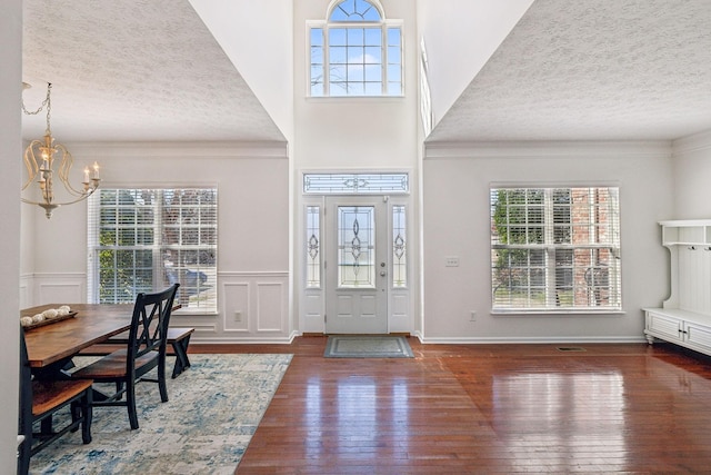 foyer with a wealth of natural light, a textured ceiling, an inviting chandelier, and hardwood / wood-style flooring