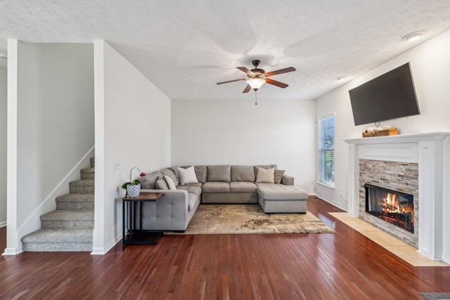 living room featuring a ceiling fan, a textured ceiling, hardwood / wood-style floors, stairway, and a fireplace