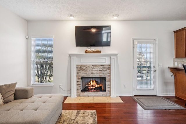 living area with a tiled fireplace, wood finished floors, baseboards, and a textured ceiling