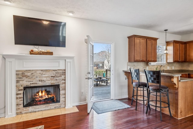 kitchen with a fireplace with flush hearth, pendant lighting, tasteful backsplash, brown cabinetry, and dark wood-style flooring