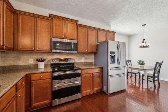 kitchen with a notable chandelier, dark wood finished floors, stainless steel appliances, brown cabinetry, and decorative backsplash