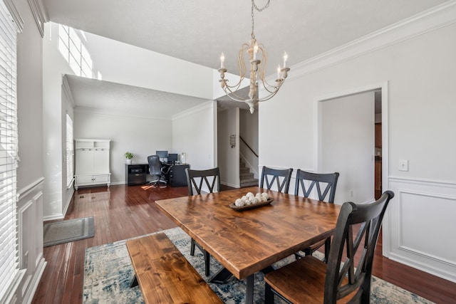 dining room featuring wood-type flooring, an inviting chandelier, crown molding, a decorative wall, and stairs