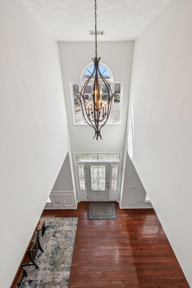 foyer featuring wood finished floors, visible vents, a high ceiling, a textured ceiling, and a chandelier