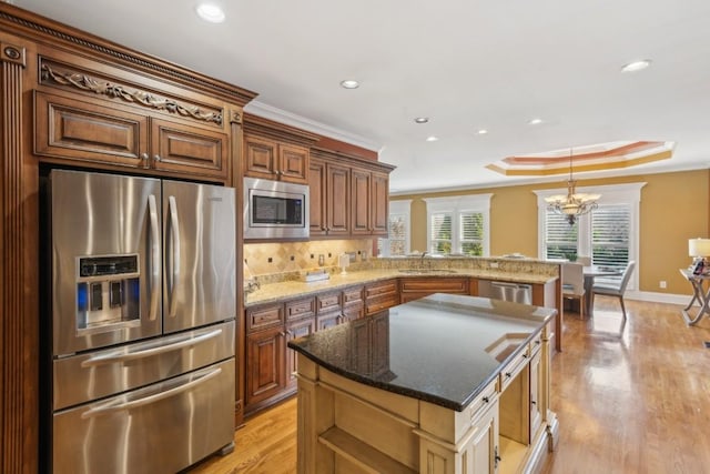 kitchen featuring ornamental molding, stainless steel appliances, a tray ceiling, and light wood-style flooring