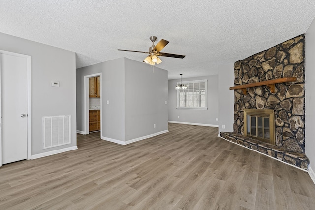 unfurnished living room featuring a fireplace, visible vents, a textured ceiling, wood finished floors, and ceiling fan with notable chandelier