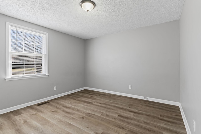 unfurnished room with baseboards, a textured ceiling, visible vents, and wood finished floors