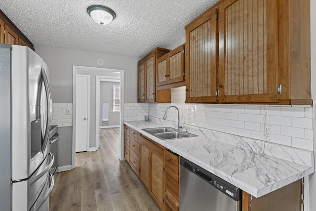 kitchen with brown cabinets, light wood finished floors, stainless steel appliances, light countertops, and a sink