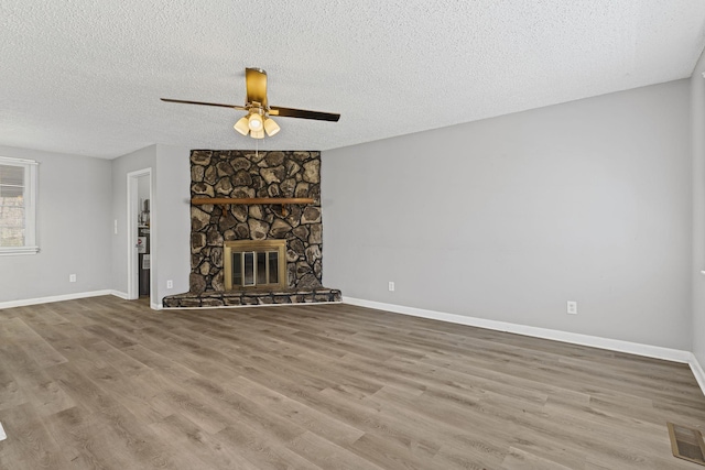 unfurnished living room featuring visible vents, a stone fireplace, a textured ceiling, and wood finished floors