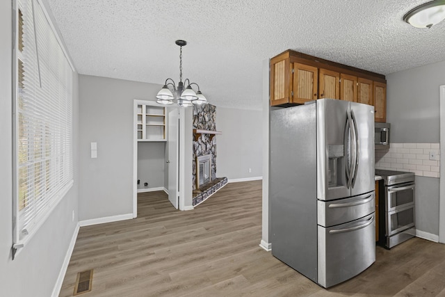 kitchen with visible vents, light wood-style flooring, appliances with stainless steel finishes, a stone fireplace, and a textured ceiling