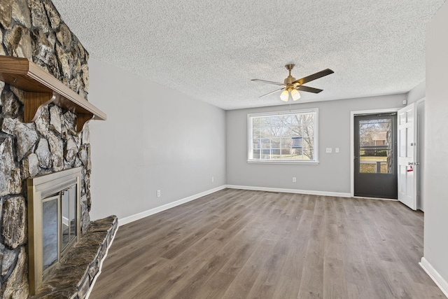 unfurnished living room featuring a textured ceiling, baseboards, wood finished floors, and a stone fireplace