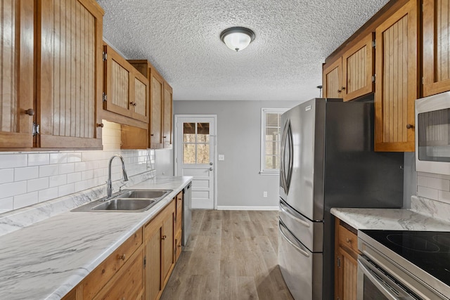 kitchen with stainless steel appliances, light wood finished floors, a sink, and light countertops