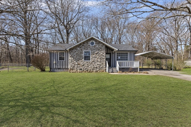 view of front of home with driveway, stone siding, a detached carport, fence, and a front yard