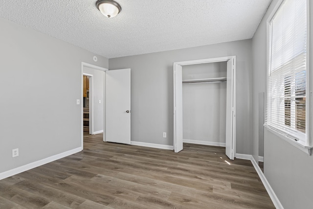 unfurnished bedroom with a closet, a textured ceiling, baseboards, and wood finished floors