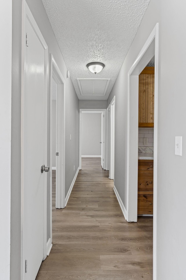 hall with light wood finished floors, attic access, baseboards, and a textured ceiling