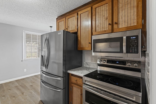 kitchen featuring brown cabinetry, appliances with stainless steel finishes, decorative backsplash, and light wood finished floors