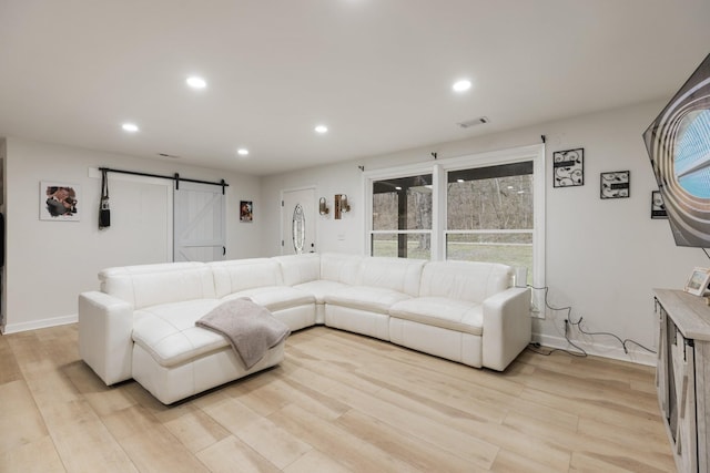 living area featuring a barn door, visible vents, baseboards, light wood-type flooring, and recessed lighting