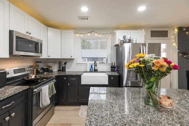 kitchen featuring visible vents, dark stone countertops, stainless steel appliances, white cabinetry, and a sink