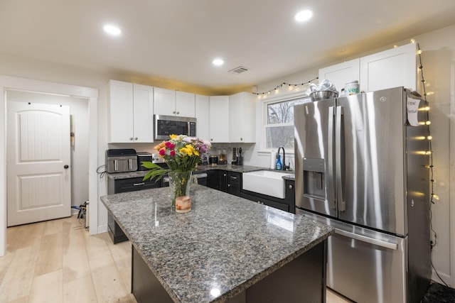 kitchen with stainless steel appliances, dark stone counters, white cabinetry, and a sink