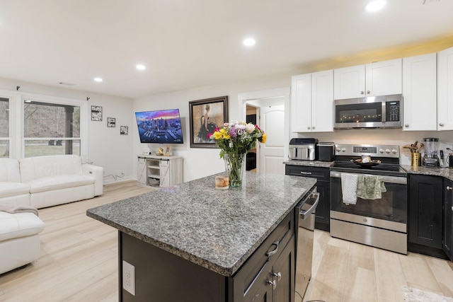 kitchen featuring recessed lighting, stainless steel appliances, a kitchen island, light wood-type flooring, and dark stone countertops