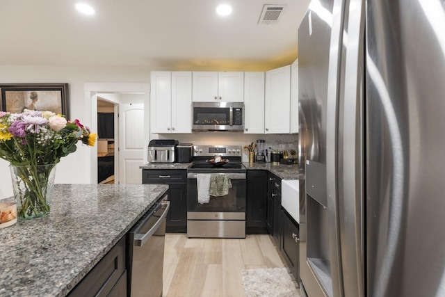 kitchen with white cabinetry, visible vents, appliances with stainless steel finishes, and dark stone counters