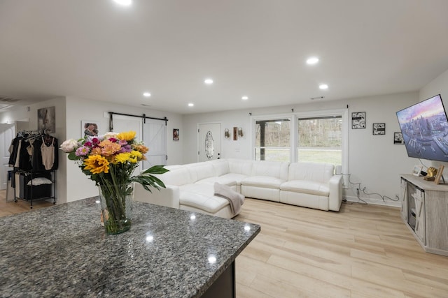 living area with a barn door, recessed lighting, visible vents, and light wood-style floors