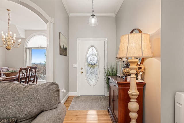 entryway with arched walkways, a notable chandelier, crown molding, light wood-style flooring, and baseboards