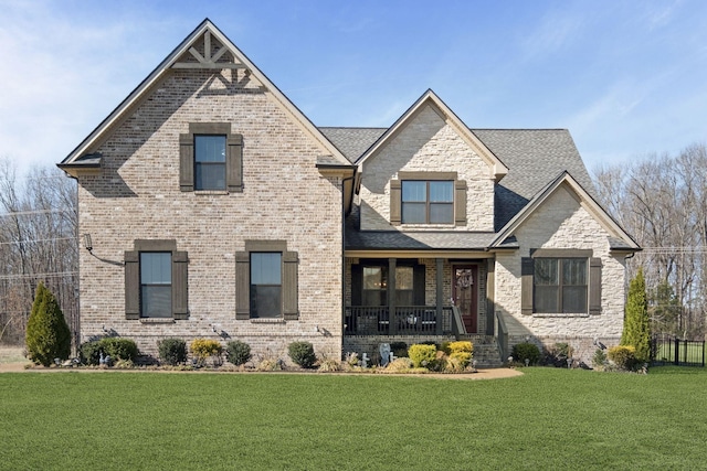 view of front facade featuring brick siding, covered porch, a front lawn, and a shingled roof