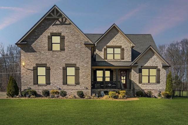 view of front of property featuring brick siding, stone siding, covered porch, and a front yard