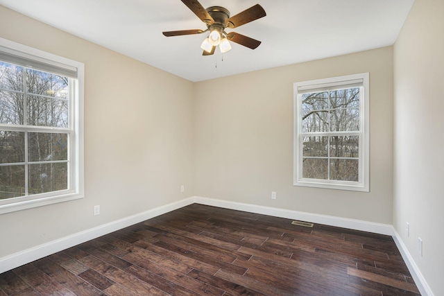 empty room with dark wood-style floors, plenty of natural light, visible vents, and baseboards