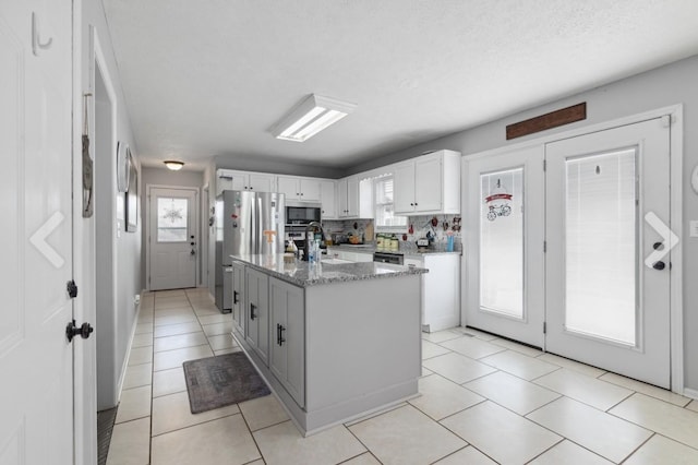 kitchen featuring stainless steel appliances, light tile patterned flooring, white cabinets, an island with sink, and light stone countertops