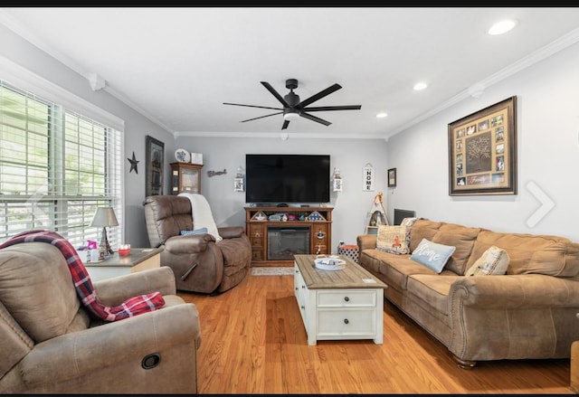 living room with ornamental molding, a glass covered fireplace, light wood-style flooring, and recessed lighting