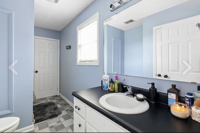 bathroom featuring toilet, vanity, baseboards, visible vents, and tile patterned floors