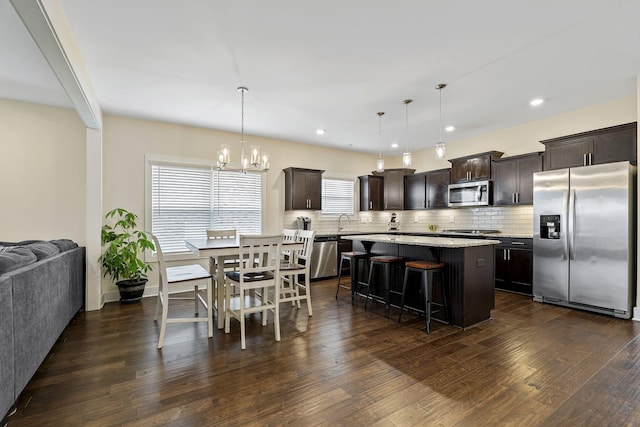 kitchen featuring a breakfast bar, dark wood finished floors, decorative backsplash, dark brown cabinets, and appliances with stainless steel finishes