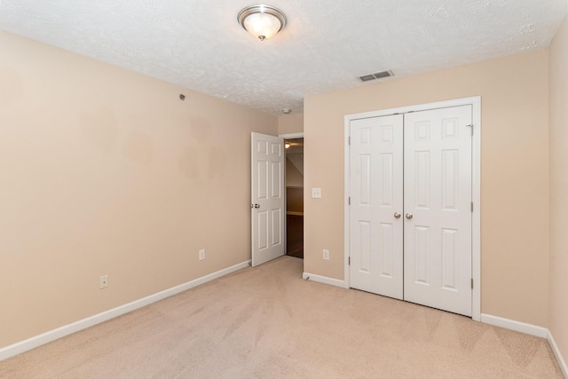 unfurnished bedroom with baseboards, visible vents, light colored carpet, a textured ceiling, and a closet