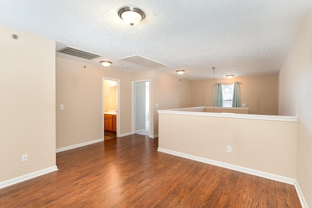 unfurnished room with dark wood finished floors, visible vents, attic access, a textured ceiling, and baseboards