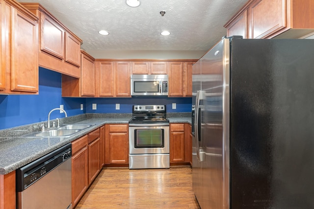 kitchen with appliances with stainless steel finishes, a textured ceiling, light wood-type flooring, a sink, and recessed lighting