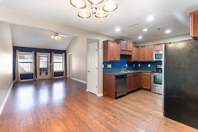 kitchen with wood finished floors, appliances with stainless steel finishes, dark countertops, and a sink