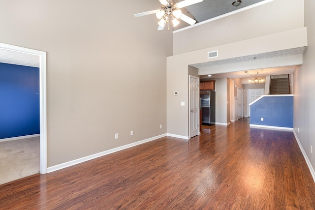 unfurnished living room with dark wood-style floors, baseboards, visible vents, and ceiling fan with notable chandelier